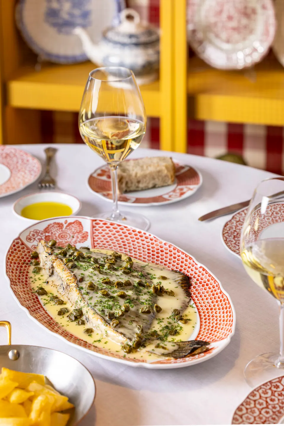 Pescado en salsa con alcaparras sobre mesa vestida con copas de vino